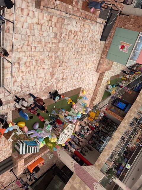 Aerial view of a lively market street with colorful stalls, umbrellas, and people walking between buildings.