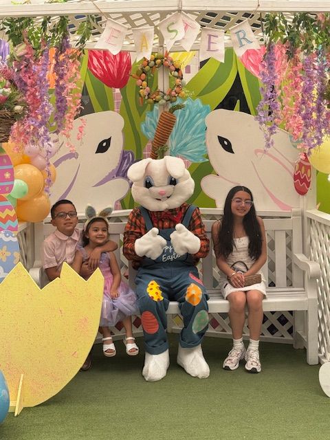 Costumed bunny mascot with three children on a bench in a colorful Easter-themed display