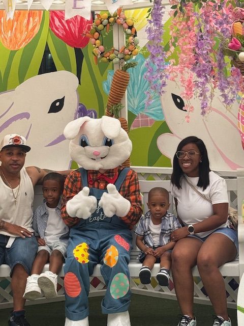 Family seated with a costumed bunny mascot in front of a colorful flower backdrop