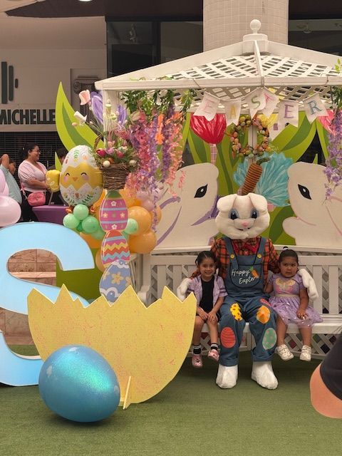 Children seated in a colorful Easter-themed display with giant bunny figures and pastel decorations