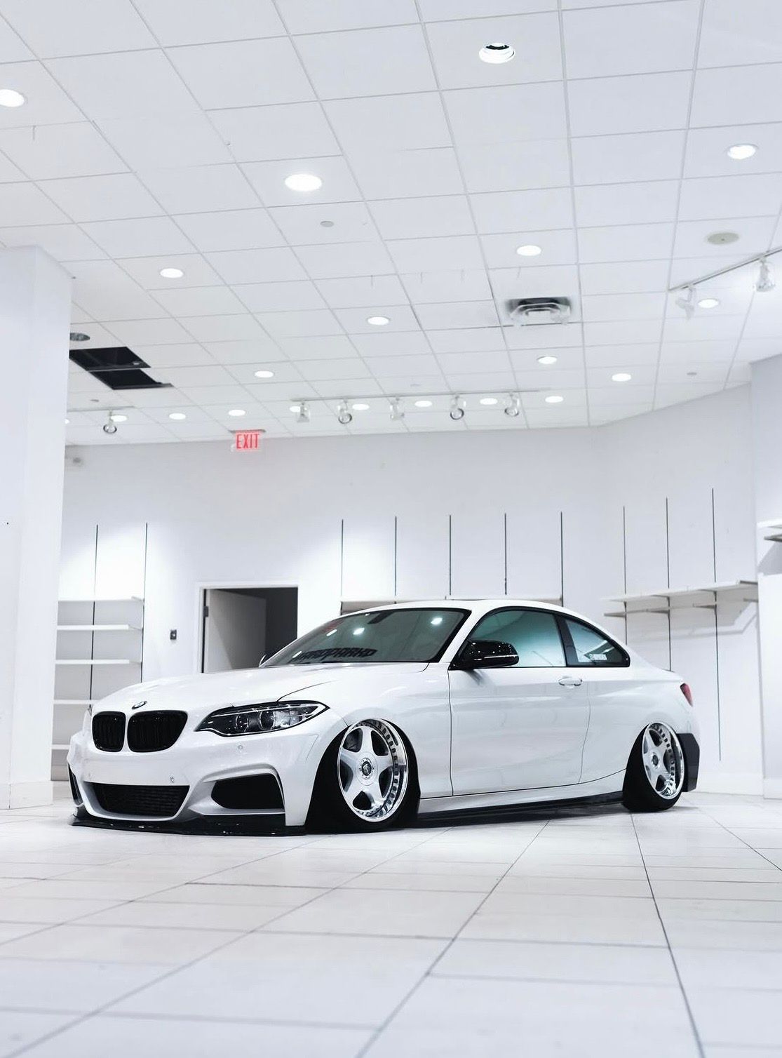 White modified BMW coupe in a bright showroom with white tiled floors and ceiling lights