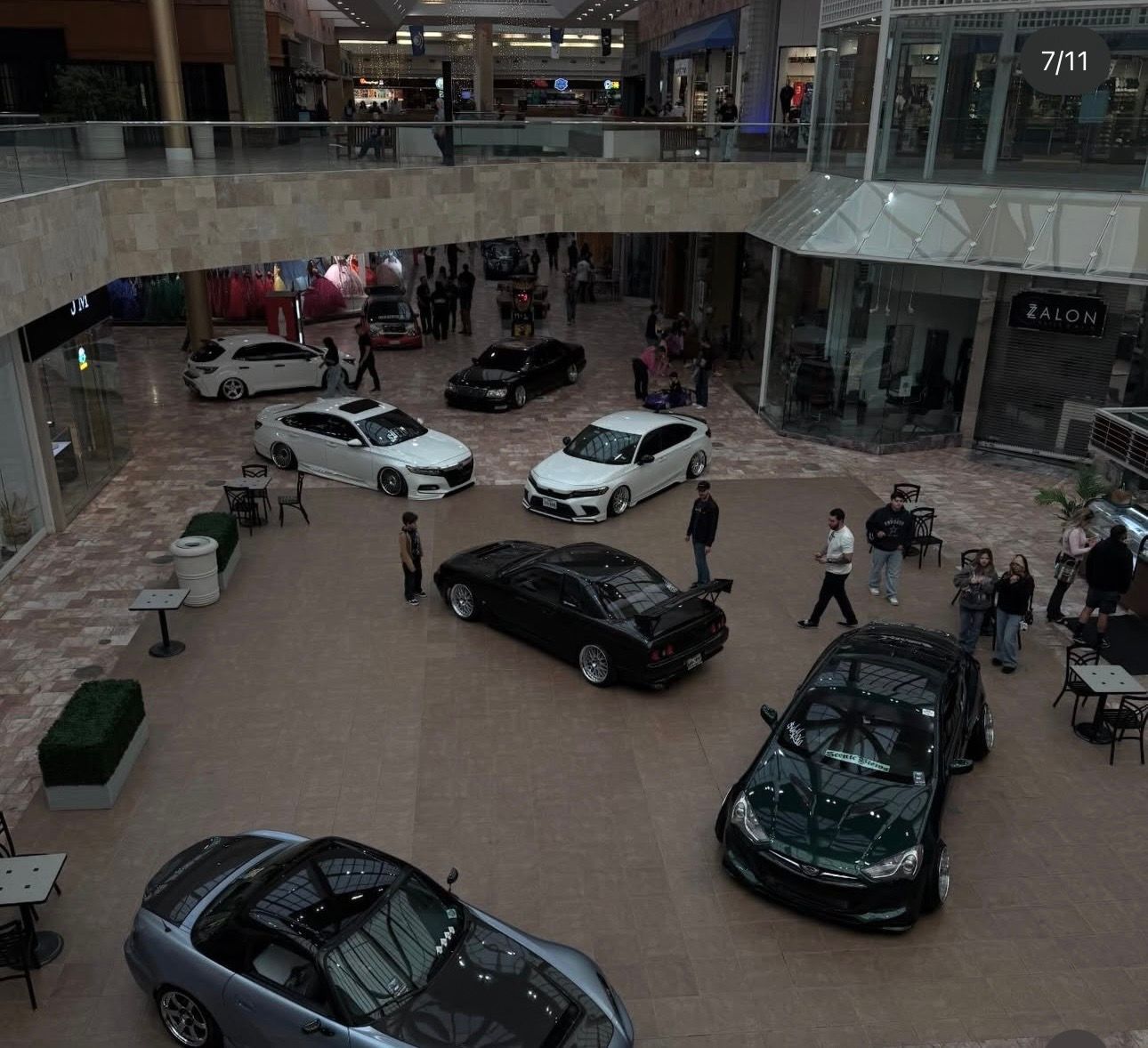 Luxury car display in a mall atrium with several sports cars on the floor and upper balcony.