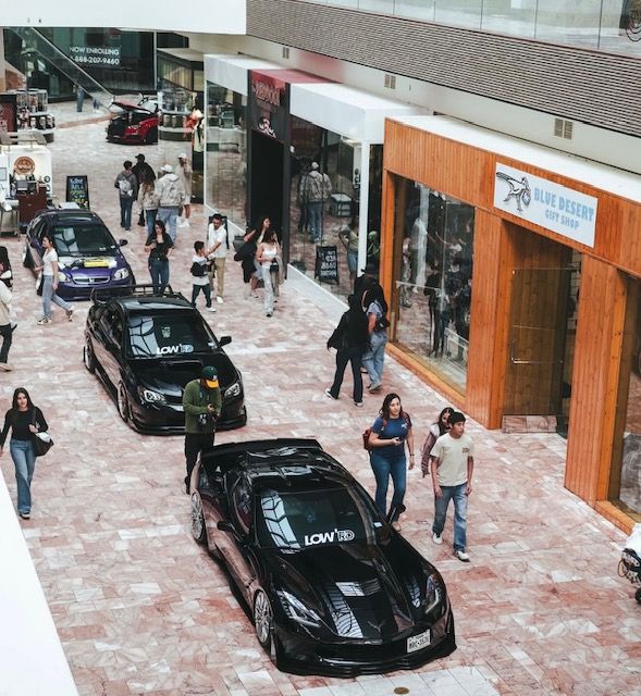 Black race cars and pedestrians in a shopping mall corridor under a covered walkway.