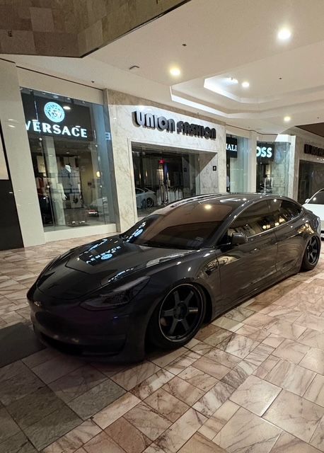 Black sports car parked in a mall hallway beside luxury storefronts, including Versace and Rolex