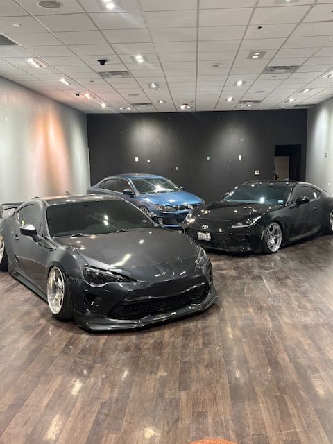 Three sports cars in a showroom, with black and blue cars on a wood floor.