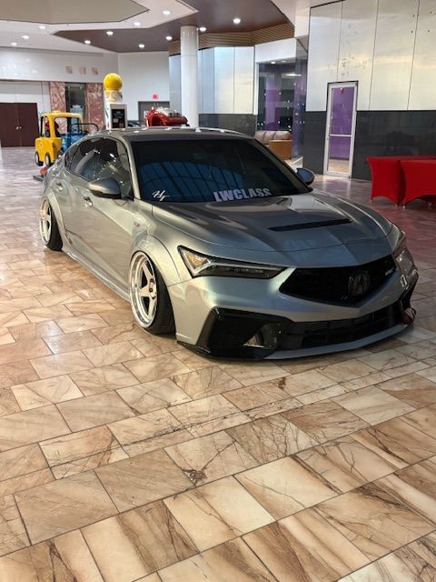 Low gray sports coupe parked indoors on a tiled floor under bright lobby lights