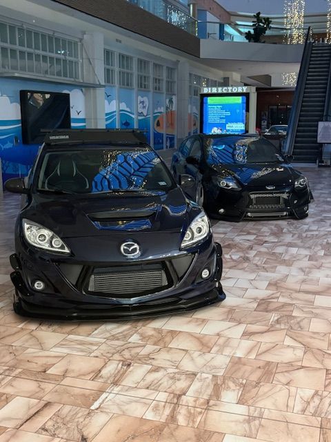 Two black Mazda sports cars displayed indoors in a showroom-like setting.