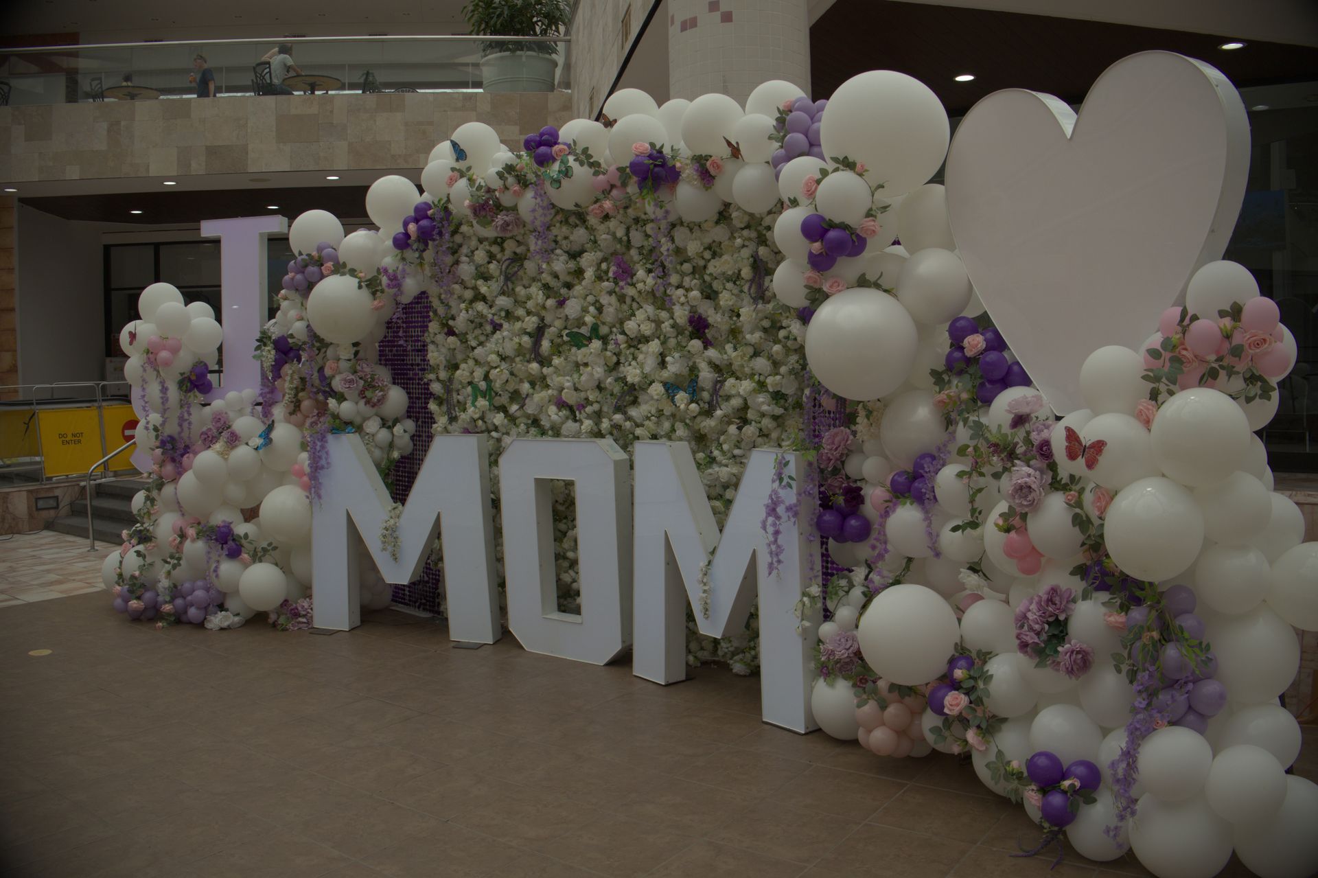 MOM balloon display with white and purple flowers and heart-shaped decorations in an indoor venue