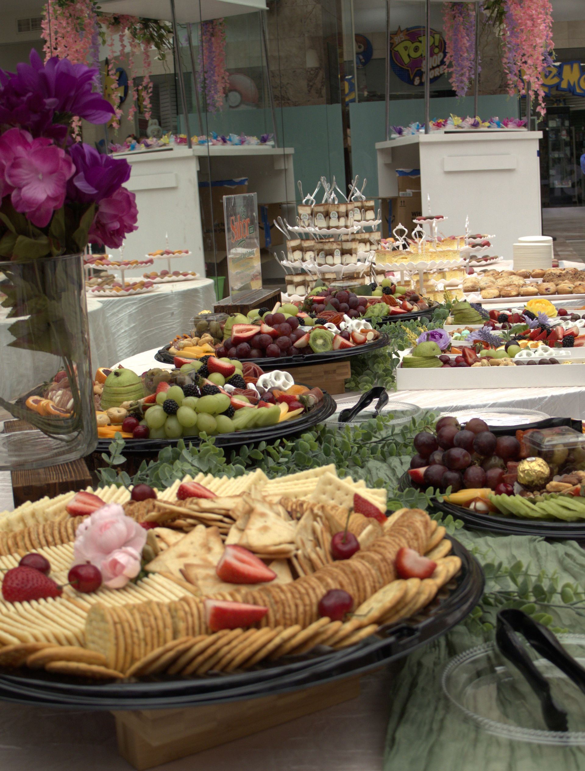 Elegant buffet table with assorted desserts, fruit platters, and floral decorations in a banquet setting