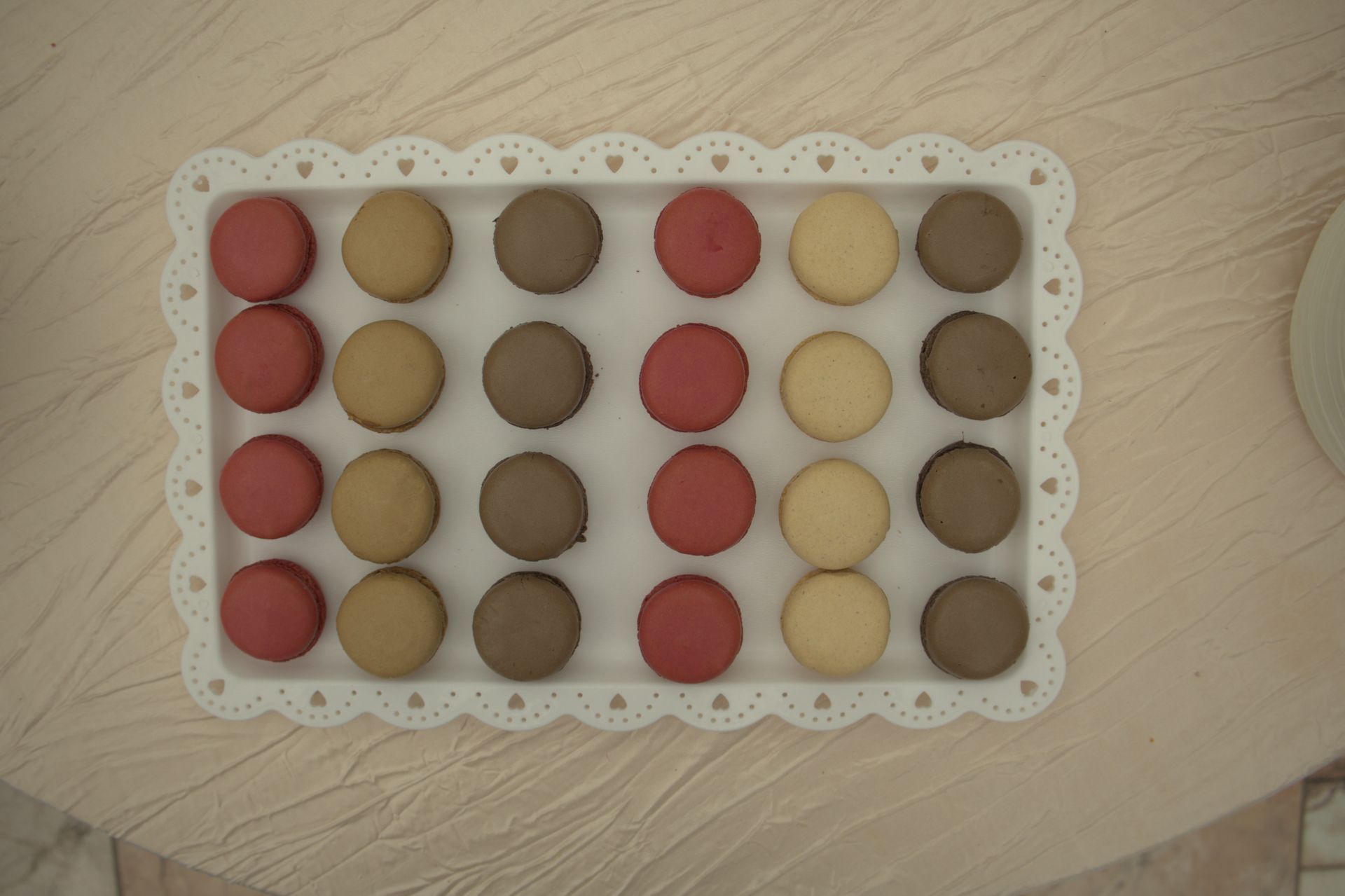 Tray of colorful round cookies or macarons arranged in neat rows on a lace-lined plate