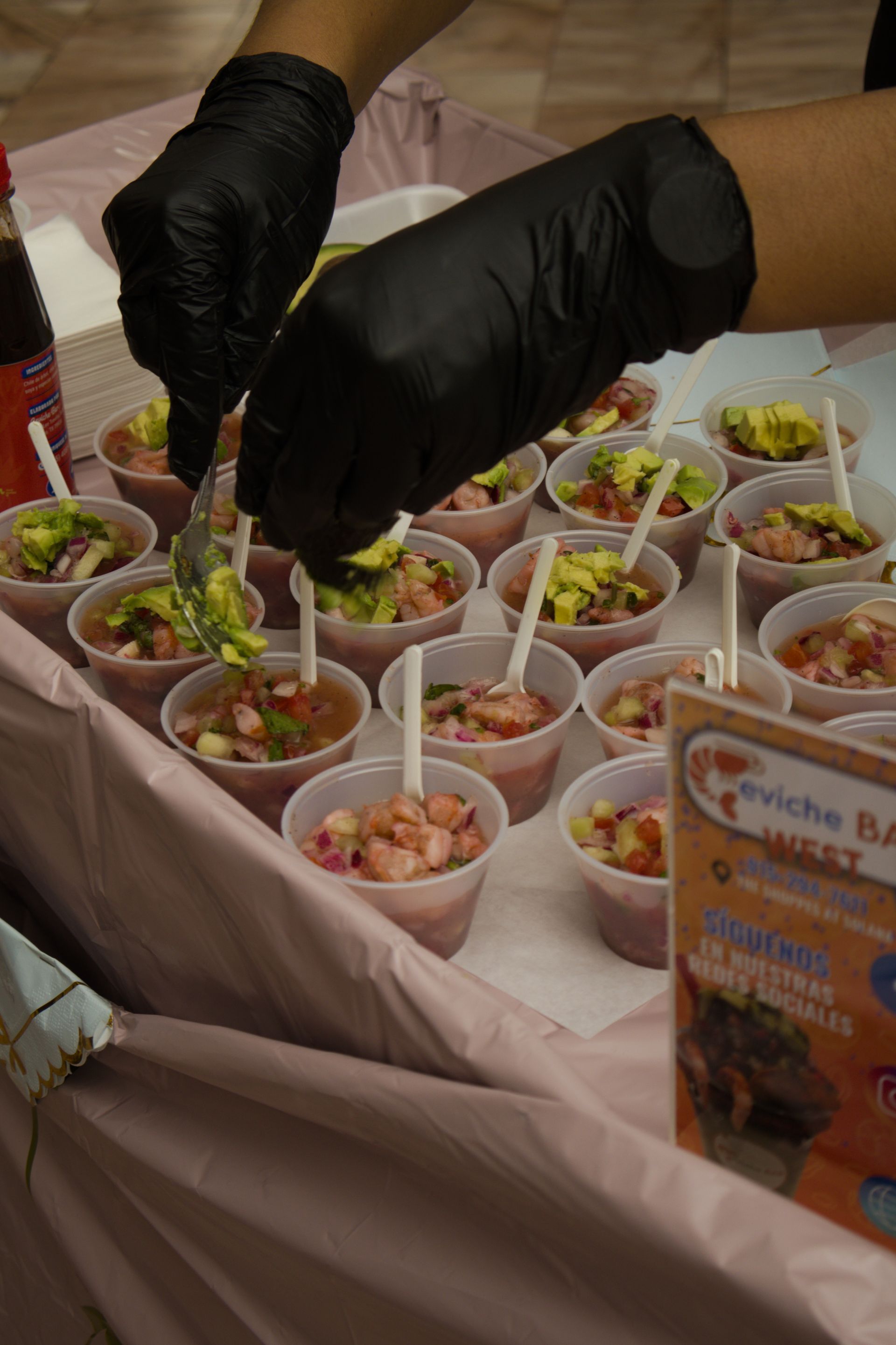 Black-gloved hands arranging small cups of food on a table at a buffet or sampling station