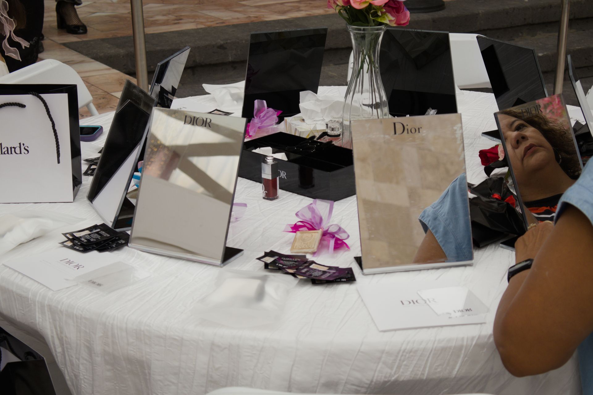 Table with mirror centerpieces, flowers, and white gift bags at an event display.