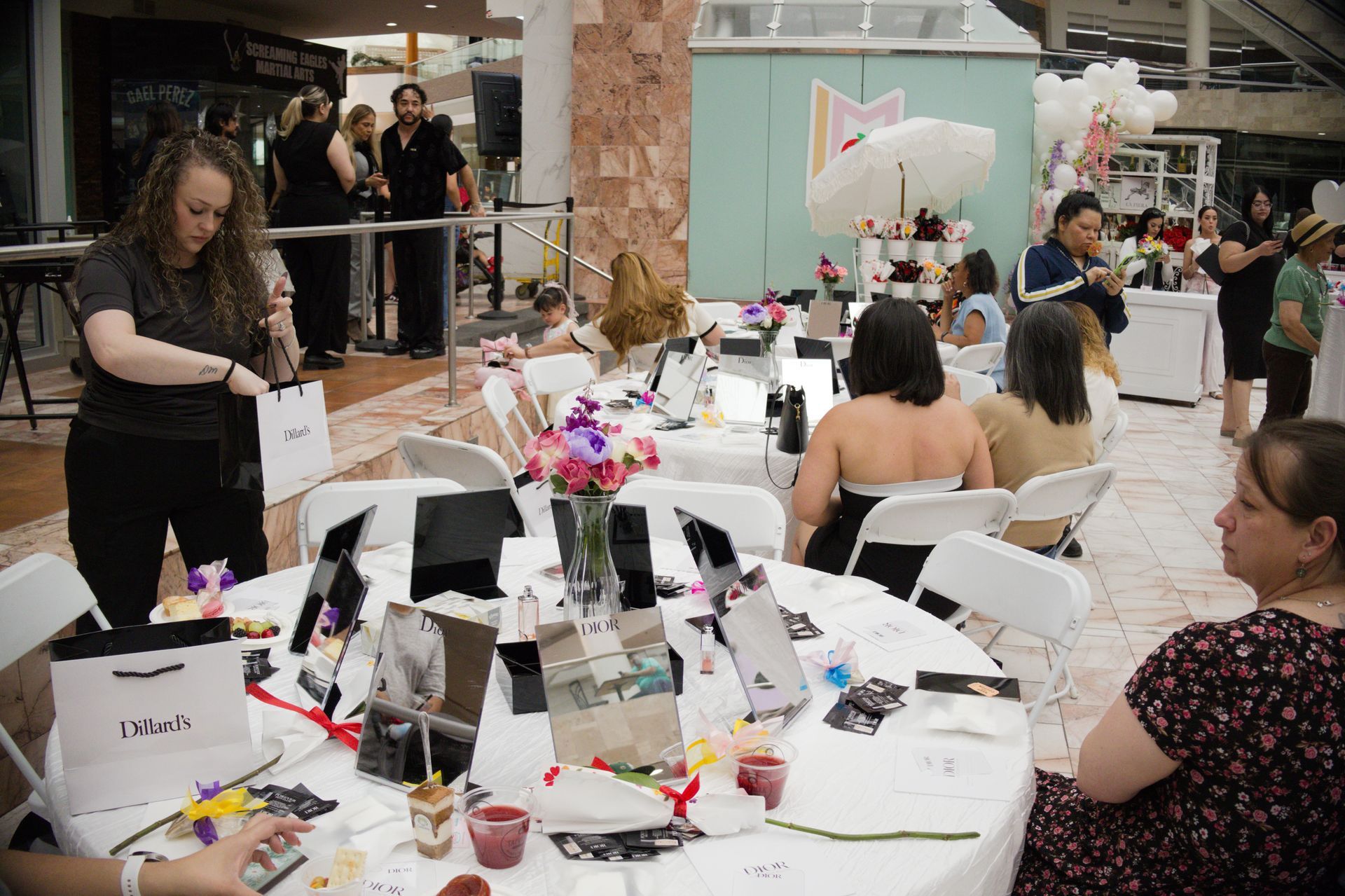 People seated at round tables in an indoor event space, with a woman arranging items on a table in the foreground