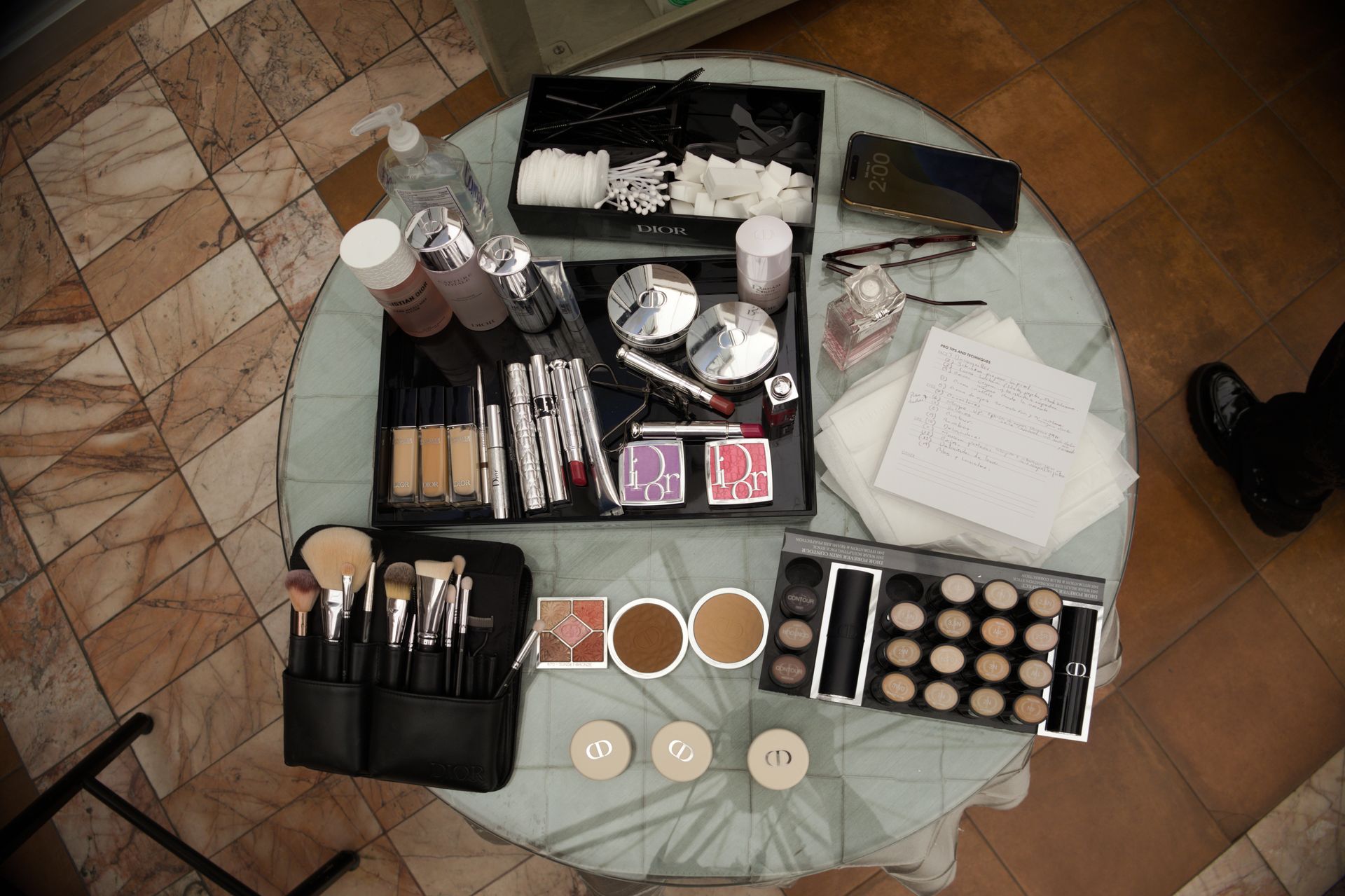 Cosmetics and makeup tools arranged on a round table with papers and a brush case