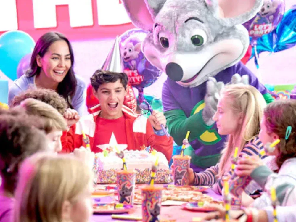 A group of children are sitting at a table at a birthday party with a chuck e cheese mascot.