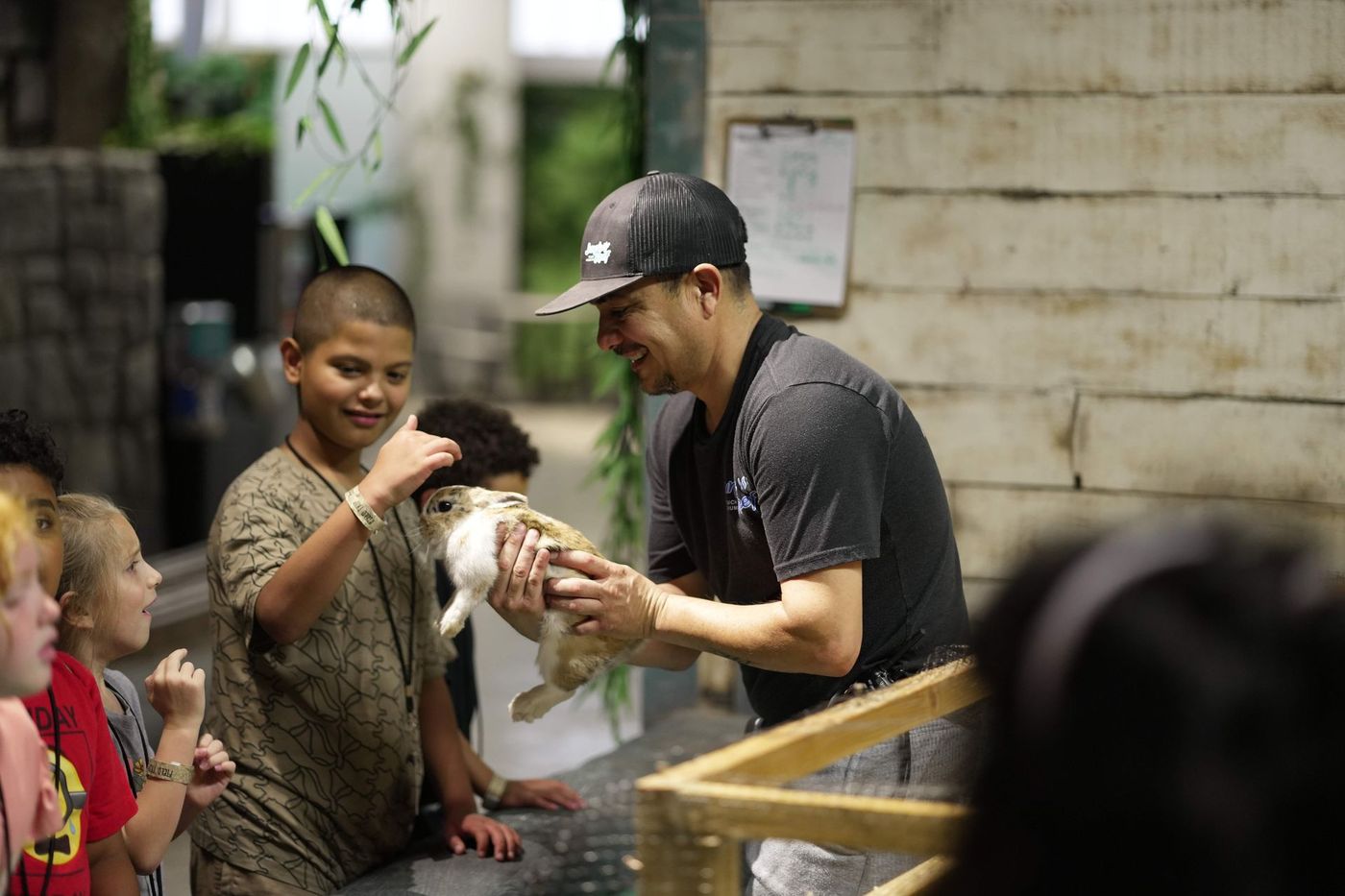 Man feeding a white rabbit while children watch at a petting zoo exhibit