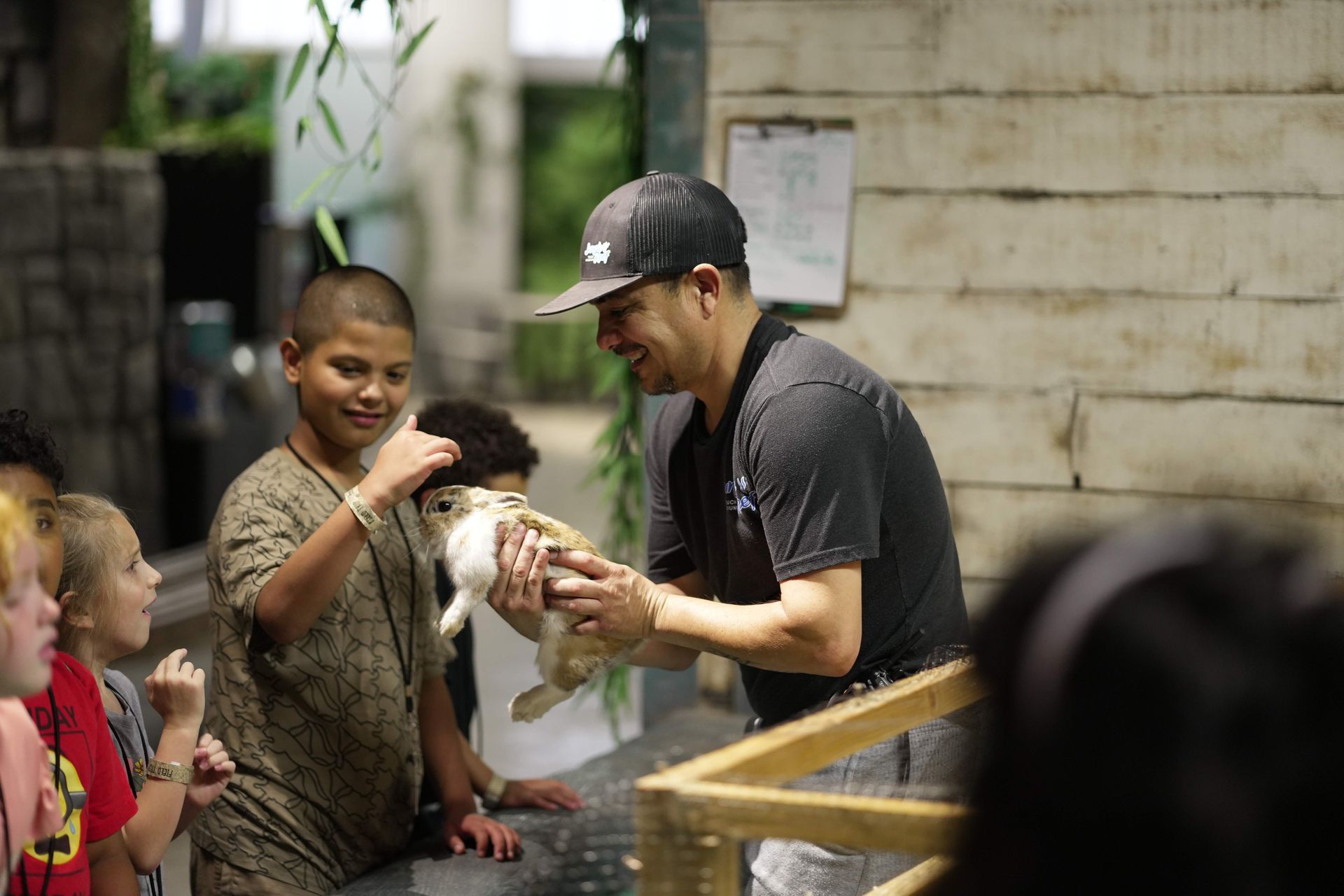 Man feeding a white rabbit while children watch at a petting zoo exhibit