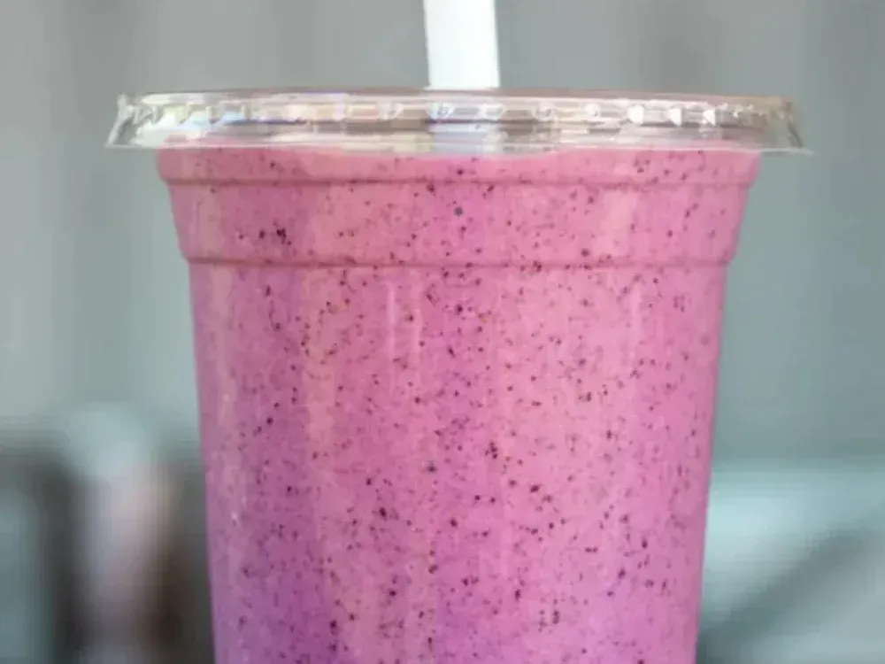 A close up of a purple smoothie in a plastic cup with a straw.