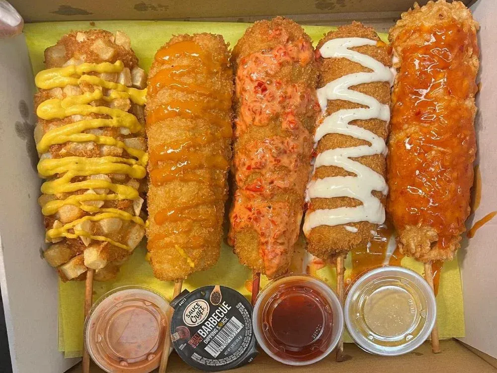 Five skewered Korean-style corndogs with assorted sauces on a tray