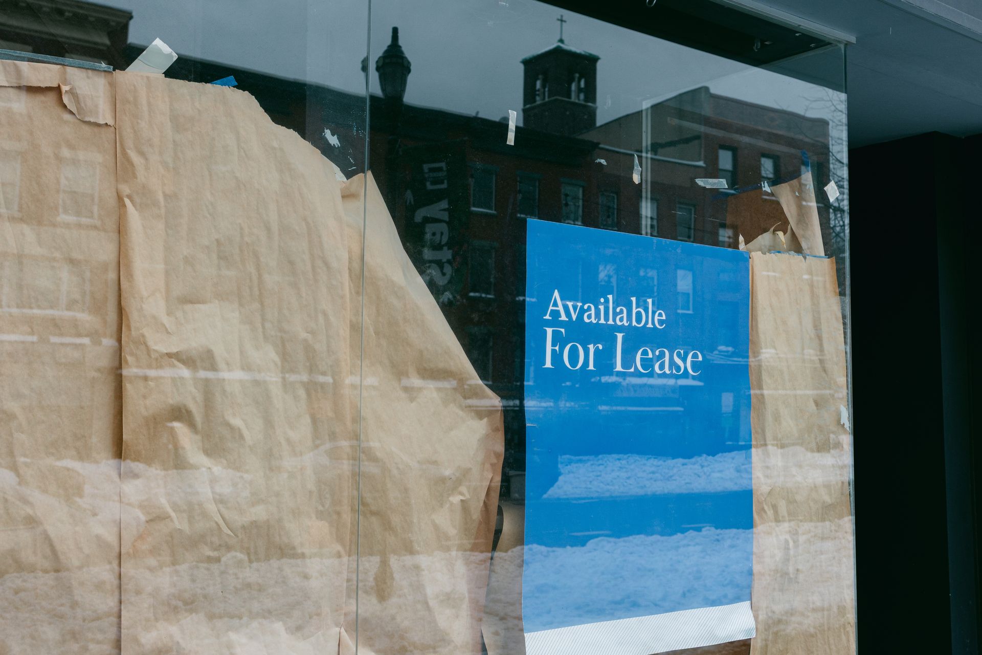Storefront window covered with paper and a blue “Available For Lease” sign.