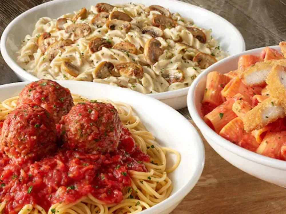 Three bowls of pasta and meatballs are sitting on a table.
