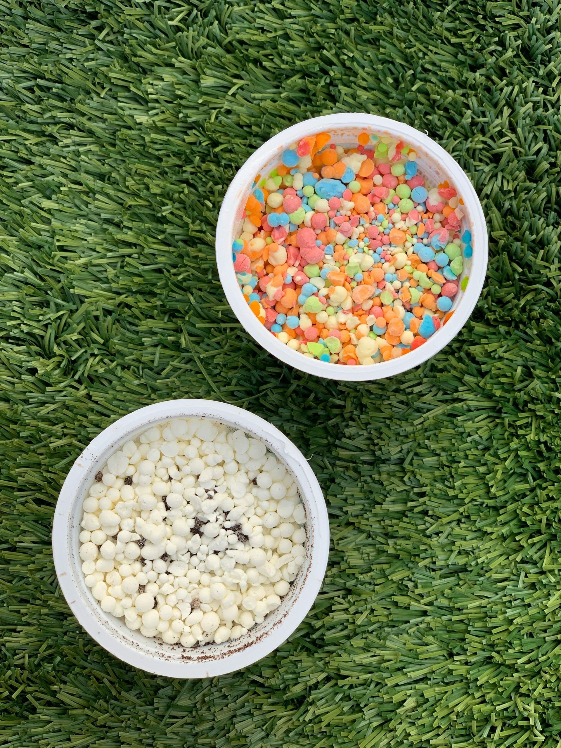 Two bowls of sprinkles are sitting on top of a green carpet.