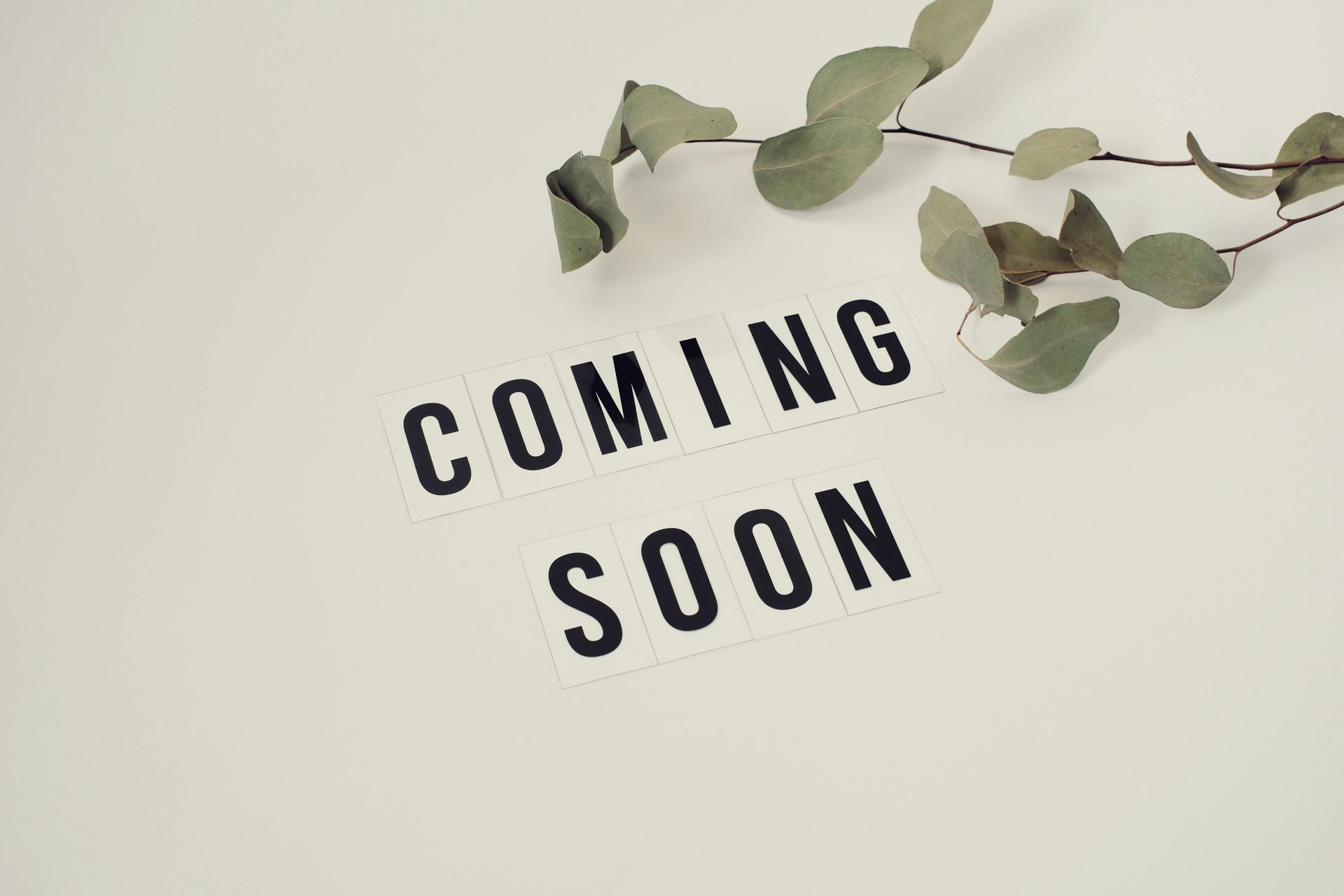 “Coming soon” text on a beige background with eucalyptus leaves at the top
