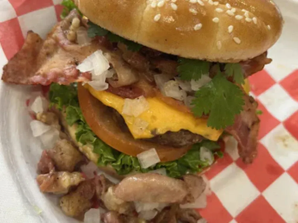 A hamburger with cheese , bacon , lettuce and tomato on a checkered napkin on a plate.