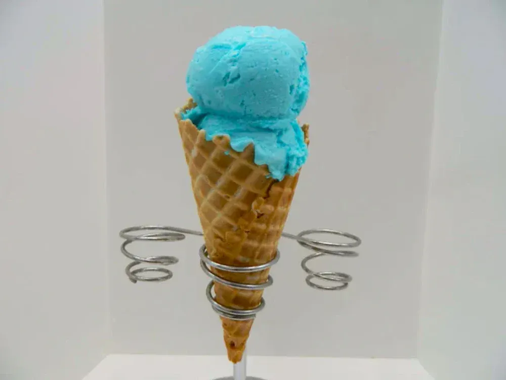 A waffle cone filled with blue ice cream on a metal stand.