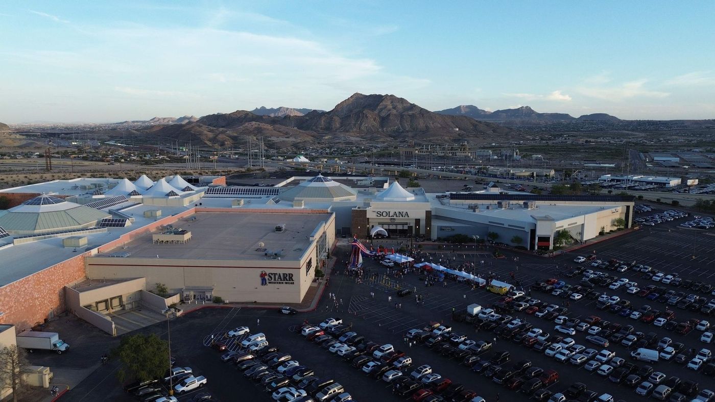 Aerial view of a large parking lot, buildings, and mountains at dusk.