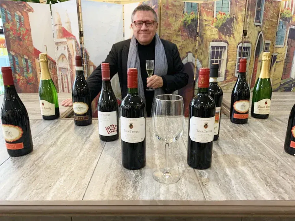 A man is sitting at a table with bottles of wine and a glass of wine.