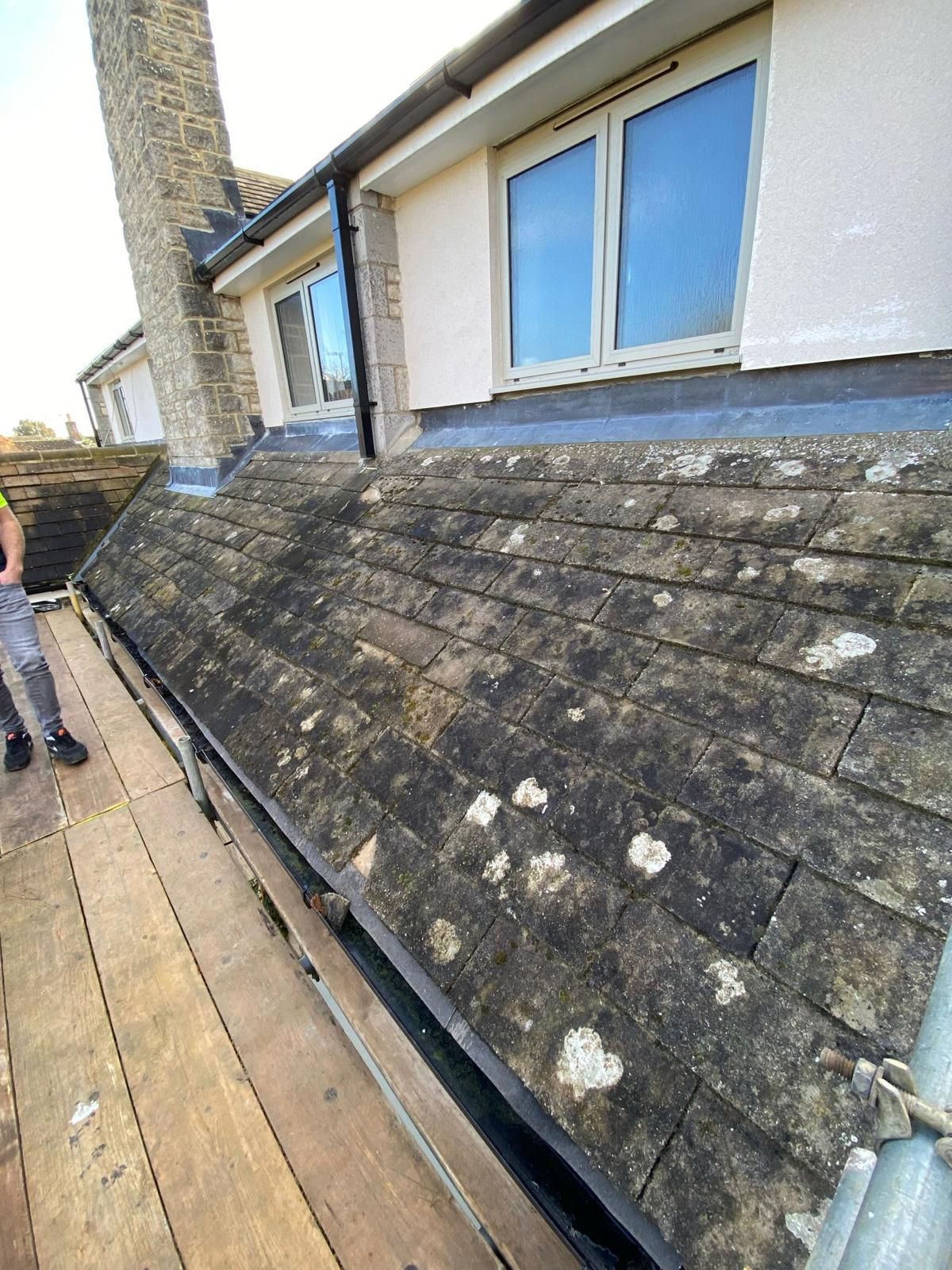 A man is standing on a wooden scaffolding next to a roof of a house.