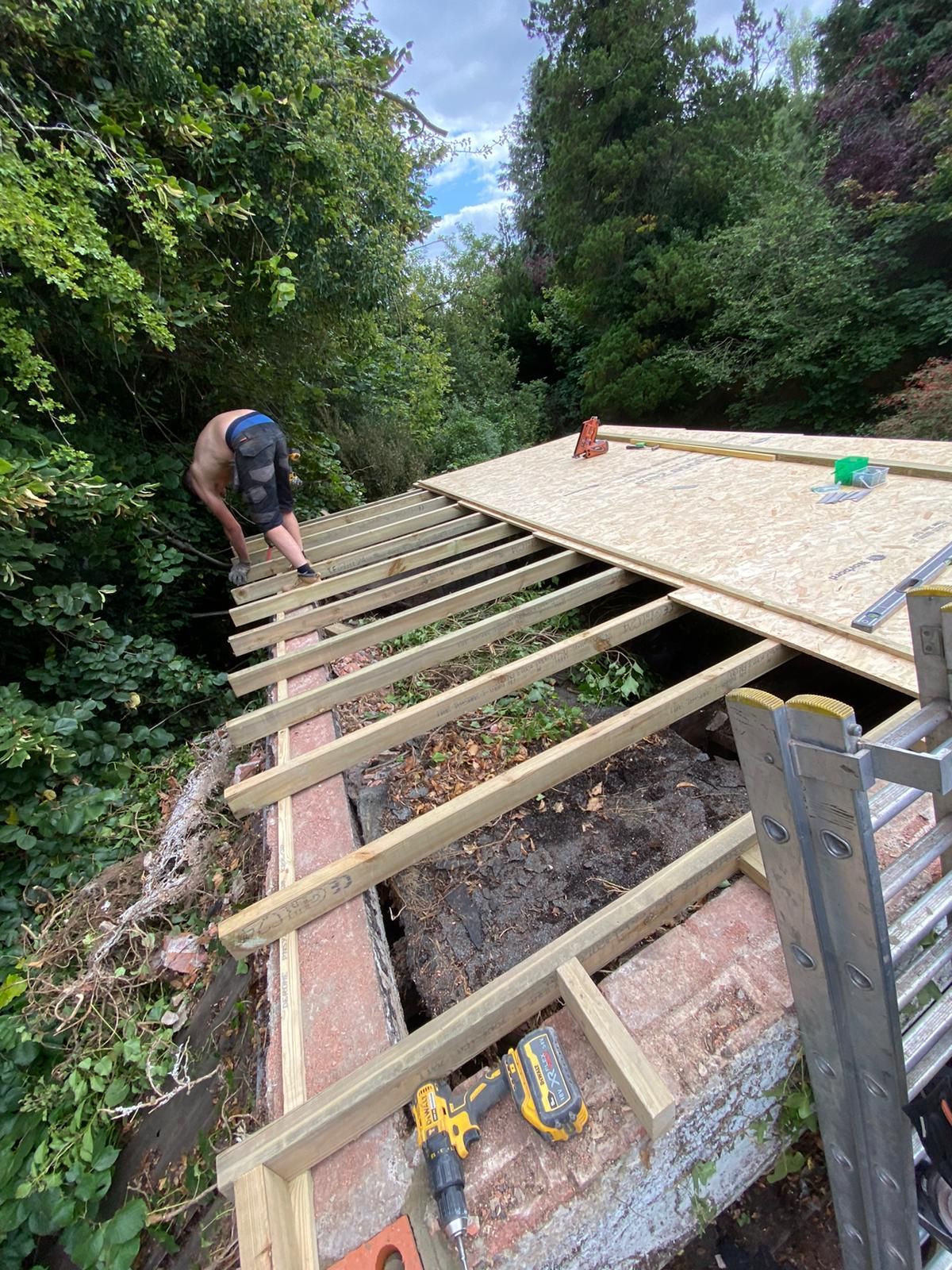 A man is working on a wooden roof installation in the woods.