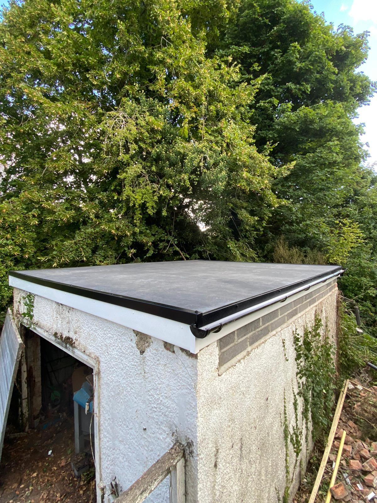 a white building with a black roof and a tree in the background
