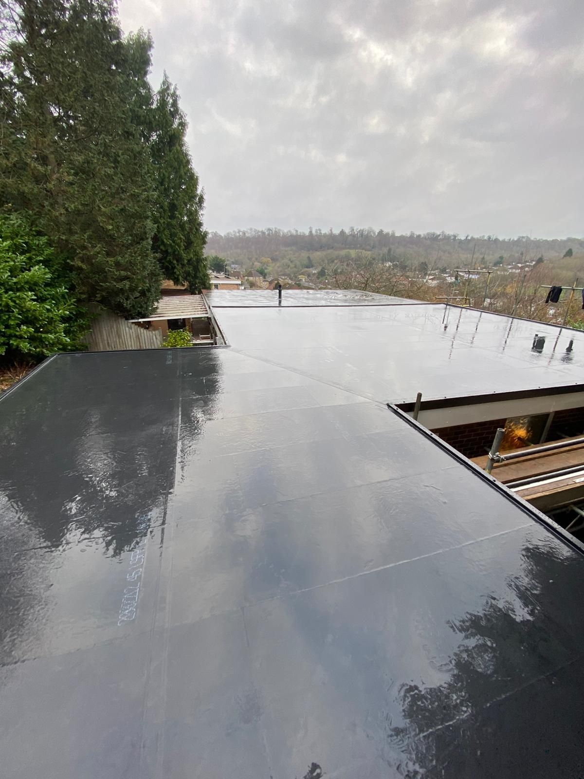A black roof with trees in the background and a cloudy sky in the background.