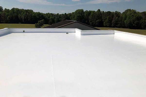 A white roof with trees in the background and a house in the background.