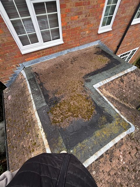 A person is standing on top of a roof next to a brick building.