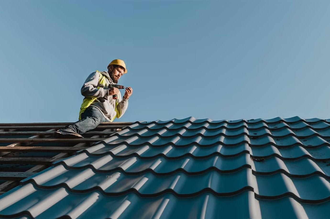 A man is standing on top of a roof holding a drill.