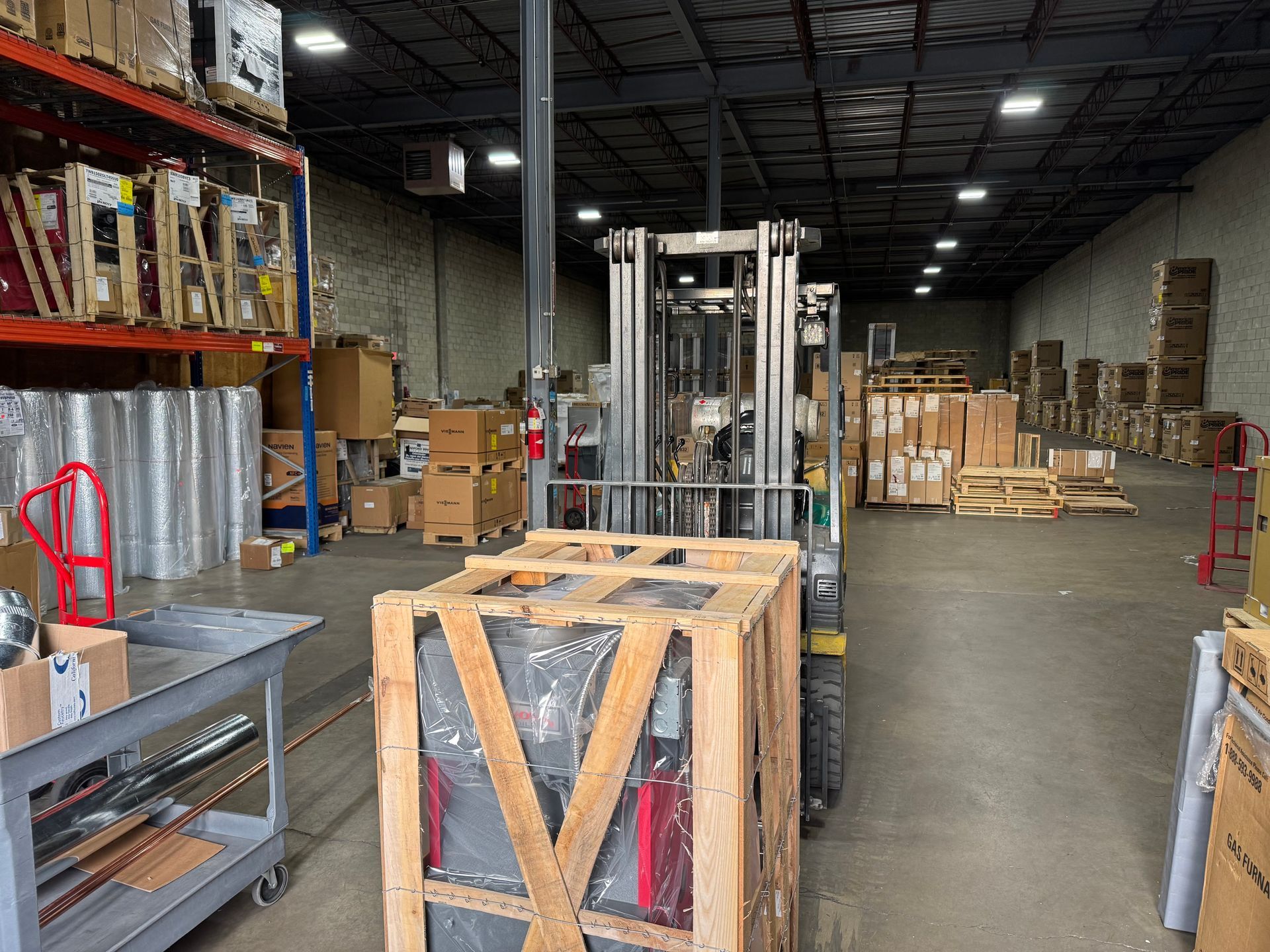 Forklift in a warehouse lifting a wooden crate, other boxes and shelves visible.