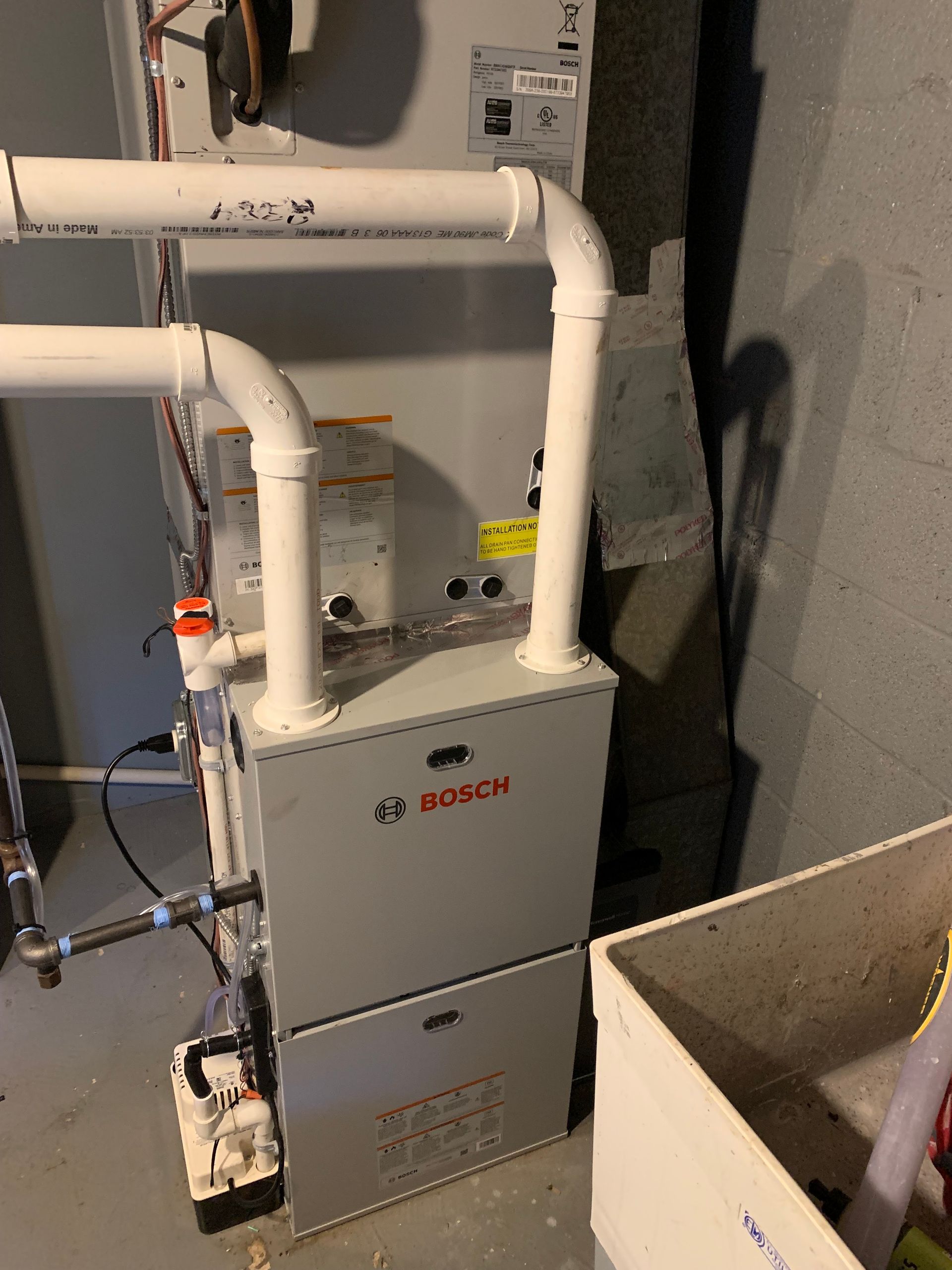 Bosch furnace in a basement, with white pipes and a utility sink nearby.