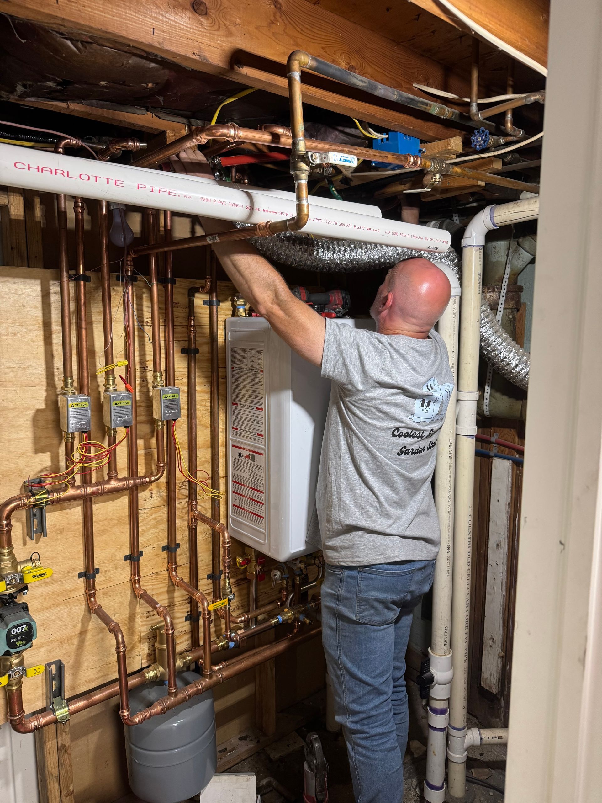 Plumber installing water heater in a basement with copper pipes and various plumbing fixtures.