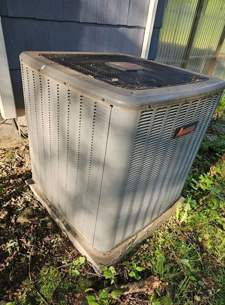 Outdoor HVAC unit beside a house, with gray metal sides and a dark top cover.