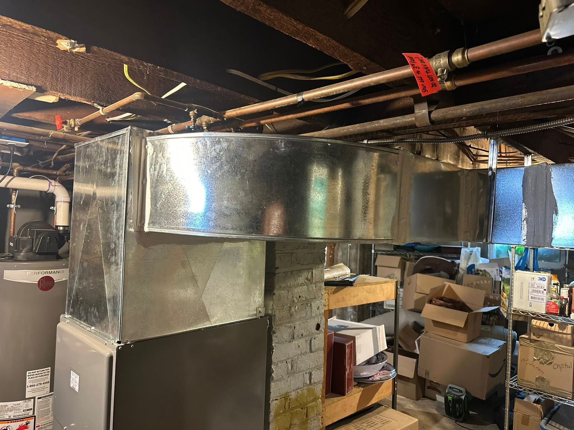 Galvanized metal ductwork in basement.  Furnace visible; boxes and storage shelves in background.