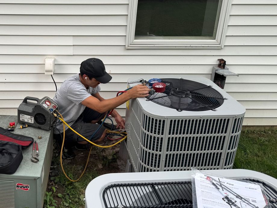 HVAC technician working on an AC unit outside a house, using gauges and tools.
