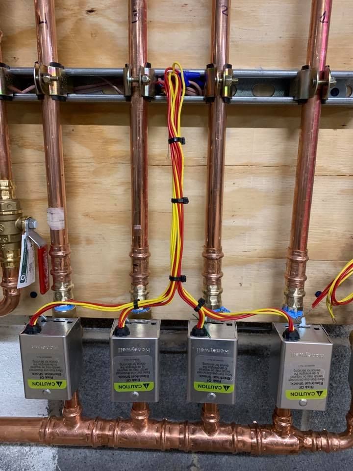 Copper pipes with connected control boxes, wiring on wooden panel.