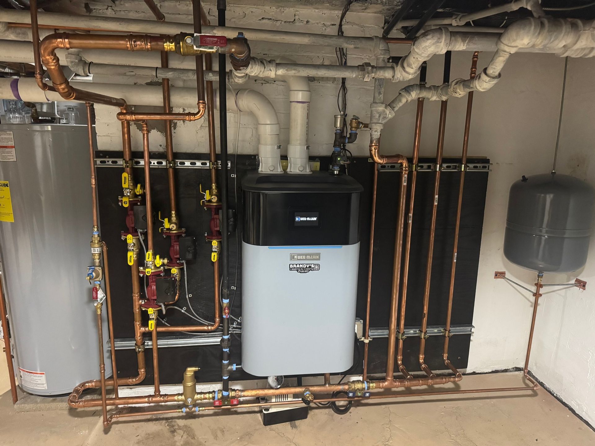 Basement with water heater, boiler, copper pipes, and expansion tank for a heating system.