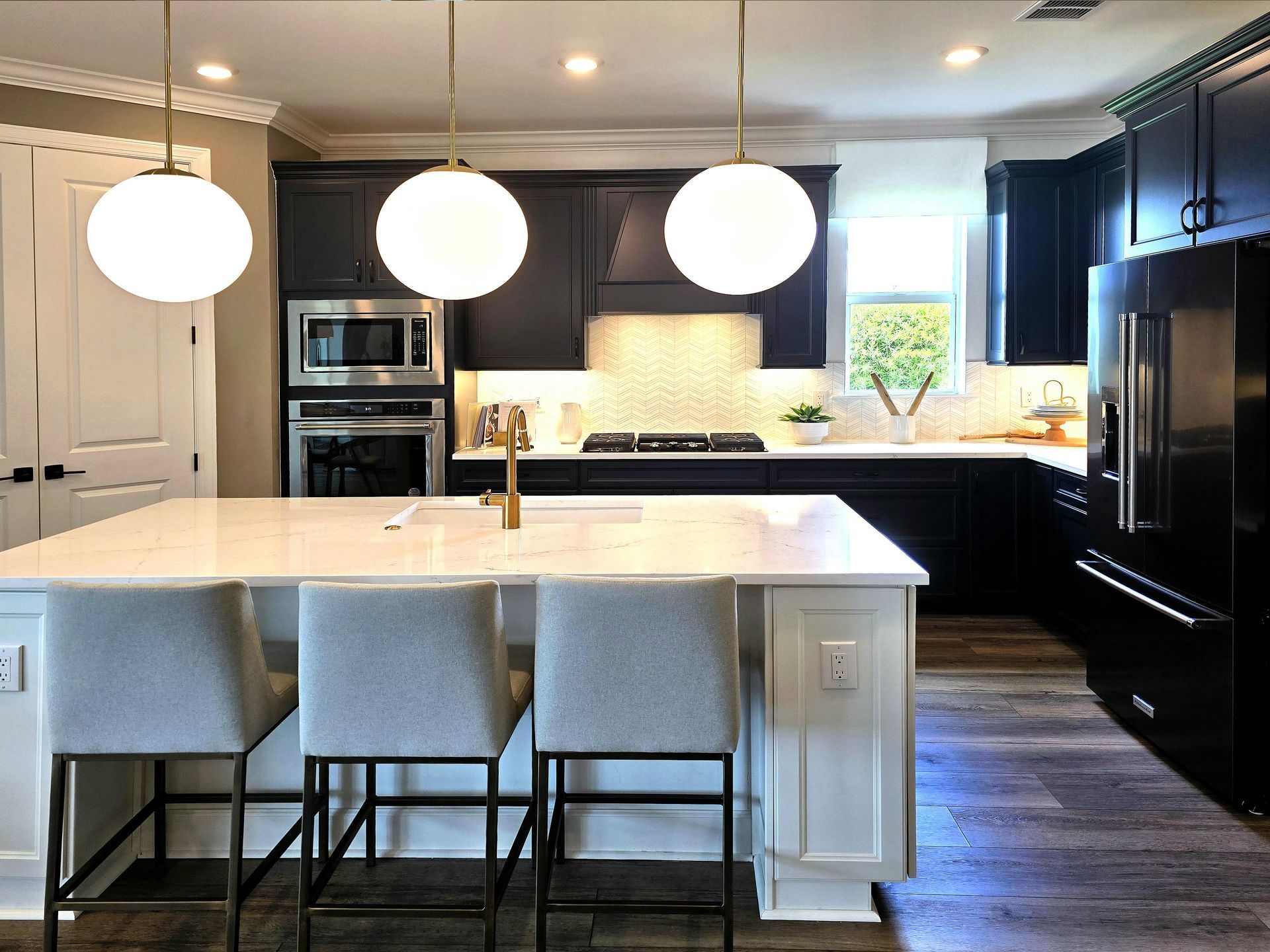 Modern kitchen with island, black cabinets, white countertops, and globe pendant lights.