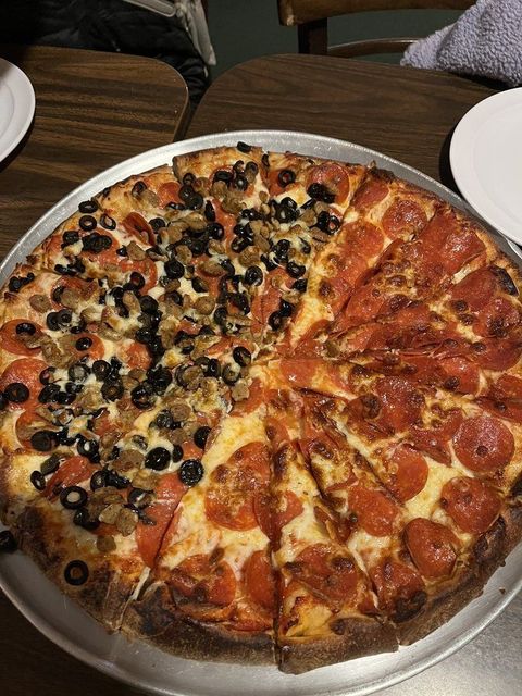 a pizza with pepperoni , olives , sausage and cheese is on a pan on a table .