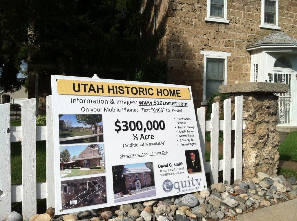 A sign for a historic home is sitting in front of a stone building.