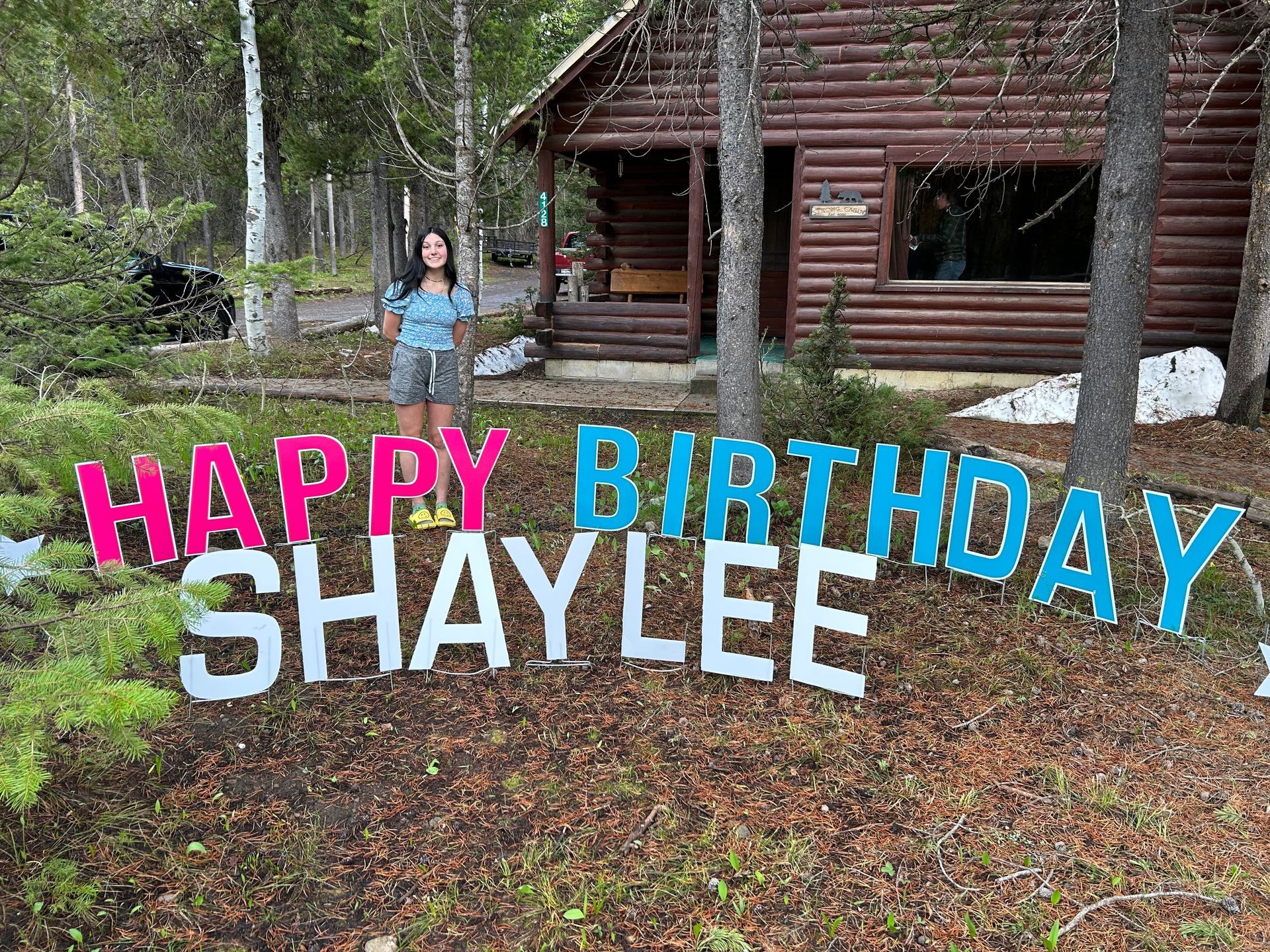 A woman is standing in front of a sign that says `` happy birthday shaylee ''.